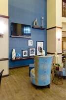 Un salón con pared azul, un televisor de pantalla plana, fotografías enmarcadas, una estantería decorativa y un sillón estampado.