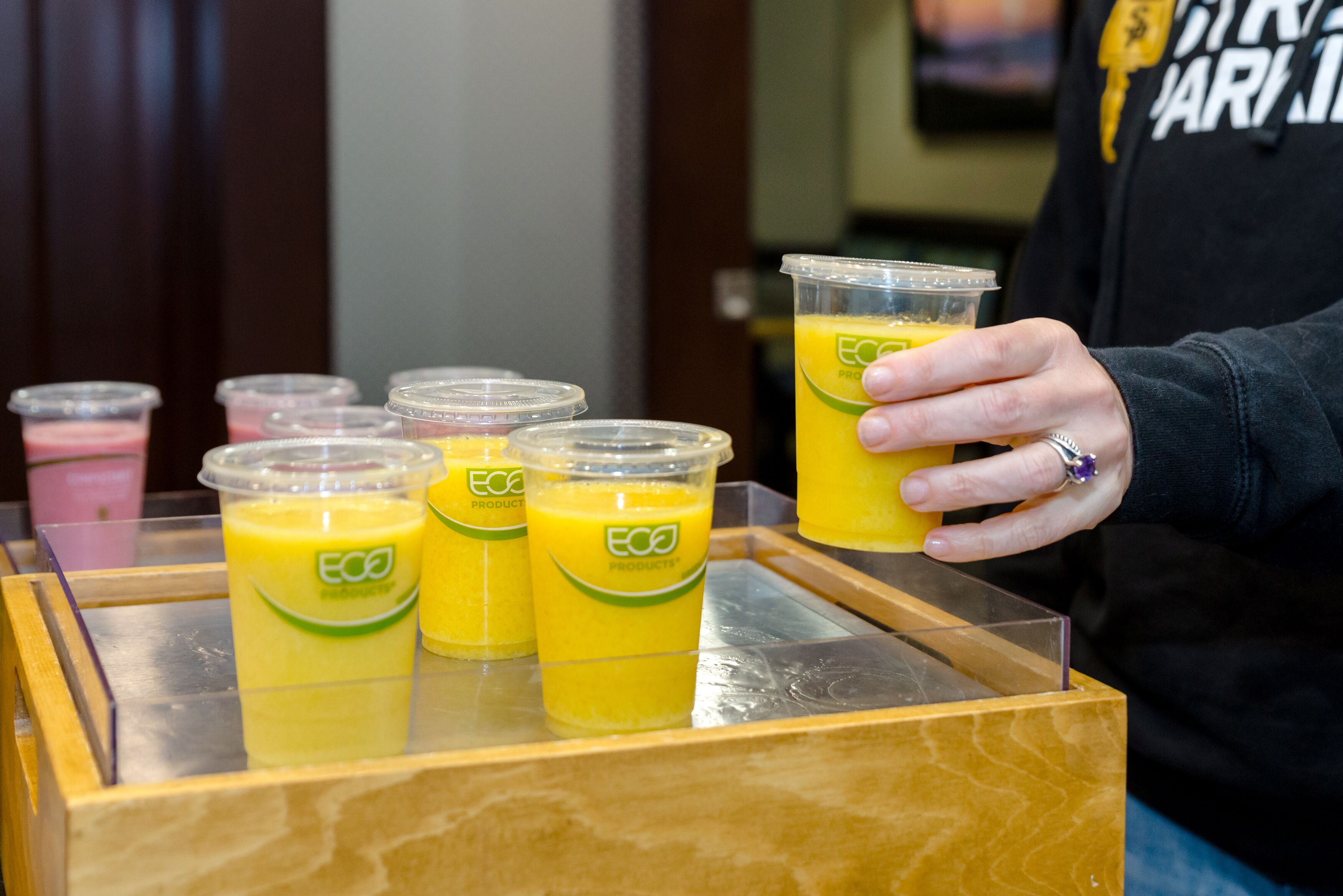 Una persona sosteniendo un vaso de jugo de naranja, con la marca 'ECO PRODUCTS' visible en el vaso.