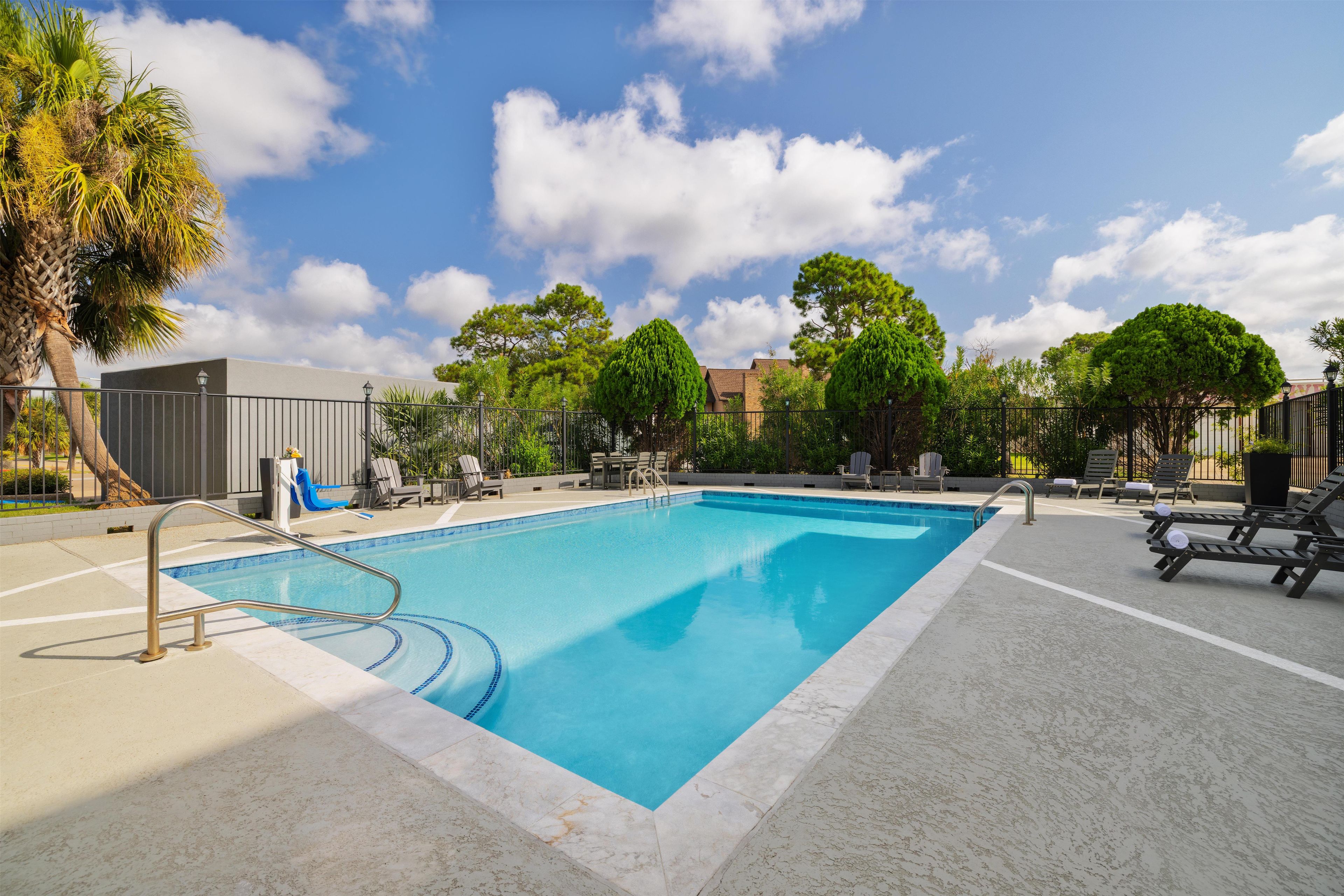 A rectangular swimming pool with a metal ladder, surrounded by lounge chairs and a paved deck.