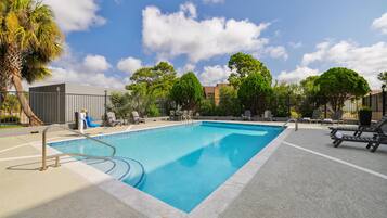 A rectangular swimming pool with a metal ladder, surrounded by lounge chairs and a paved deck.