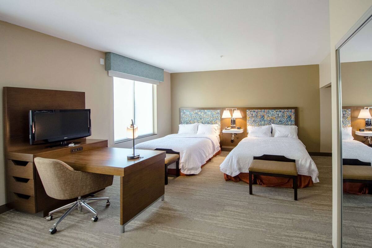 A hotel room with a desk, two beds, a TV, and a bathroom.