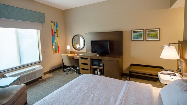 A hotel room with a bed, desk, TV, and a window with blinds. - Hampton Inn & Suites Port Arthur (Port Arthur)