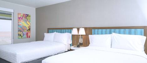 A hotel room with two beds, a nightstand with a lamp, and a colorful abstract painting on the wall.