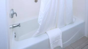 A modern bathroom with a white bathtub, a showerhead, a grab bar, and a white towel on the edge.