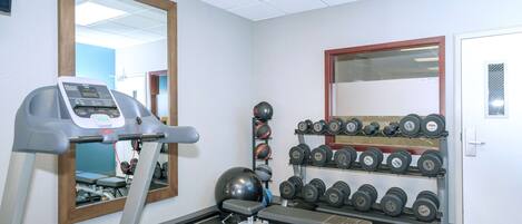 A gym with a treadmill, weights, and a mirror.