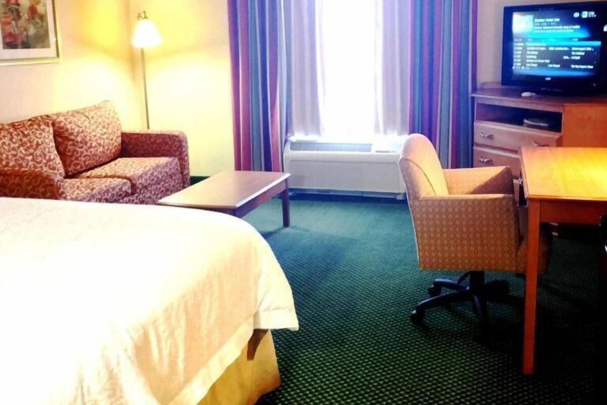A hotel room with a bed, a desk, a chair, a television, and a window with curtains.