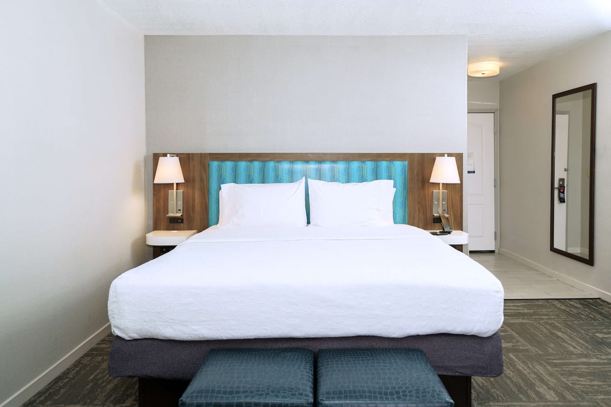 A hotel room with a large bed, two bedside tables with lamps, a wooden headboard, and a mirror on the wall.