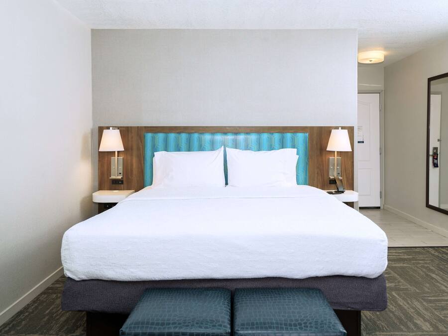 A hotel room with a large bed, two bedside tables with lamps, a wooden headboard, and a mirror on the wall.