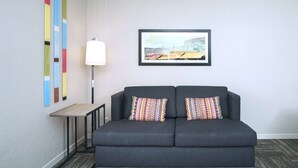 Un divano grigio scuro con cuscini colorati e decorati, un quadro raffigurante una veduta cittadina sopra di esso, e una lampada da terra alta alla sinistra.