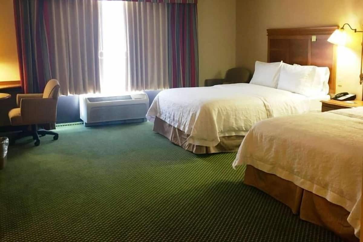A hotel room with two beds, a desk, a chair, and a window with curtains.
