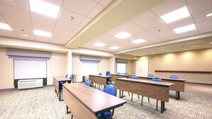 Una sala conferenze con diversi tavoli e sedie, uno schermo per proiezioni e un pavimento rivestito di moquette.