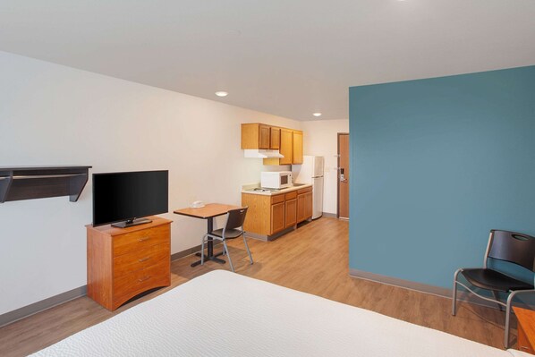Habitación de hotel compacta con cama, escritorio, televisor, kitchenette y baño.