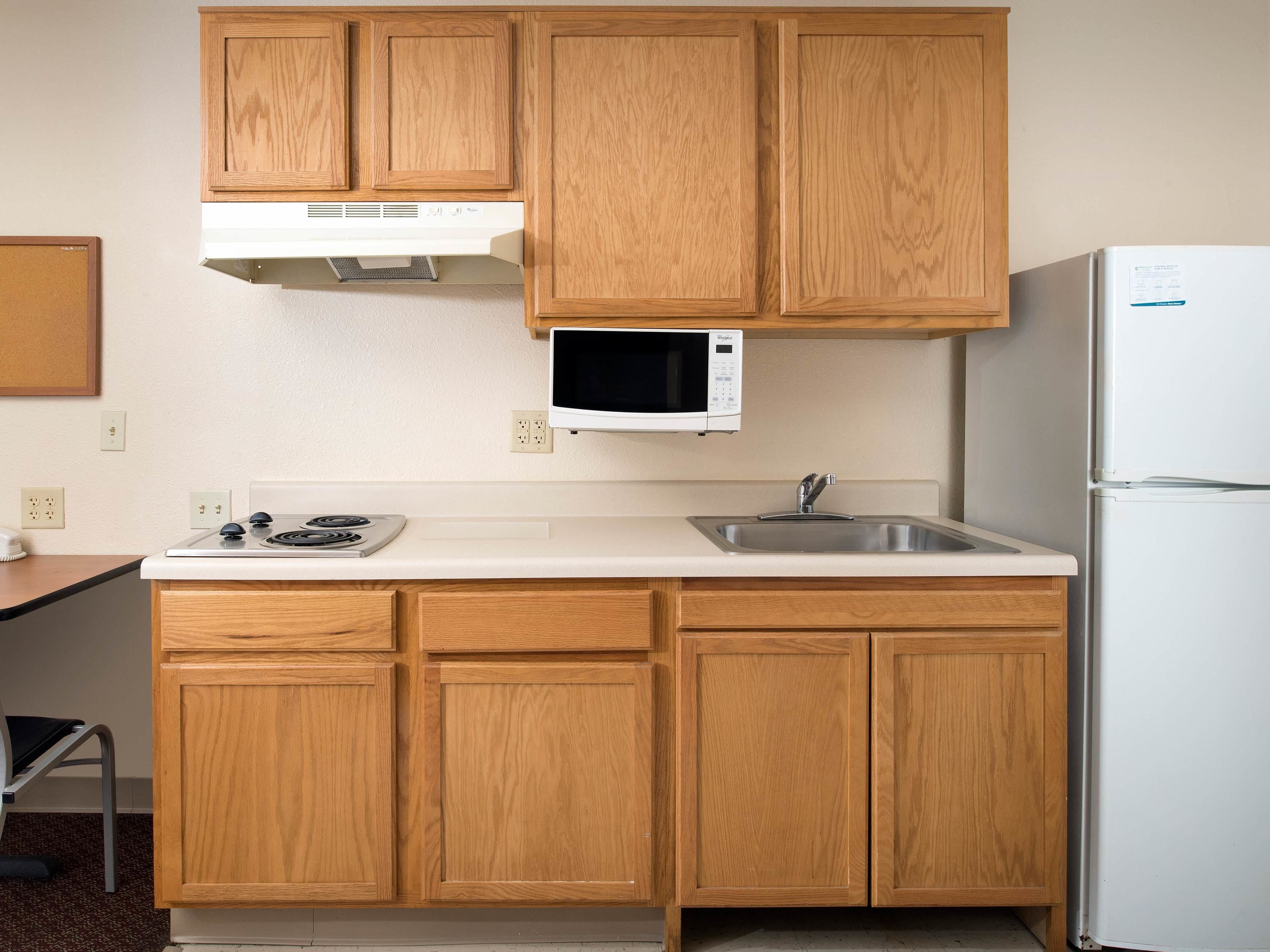 A kitchen with wooden cabinets, a microwave, a stove, a sink, and a refrigerator.