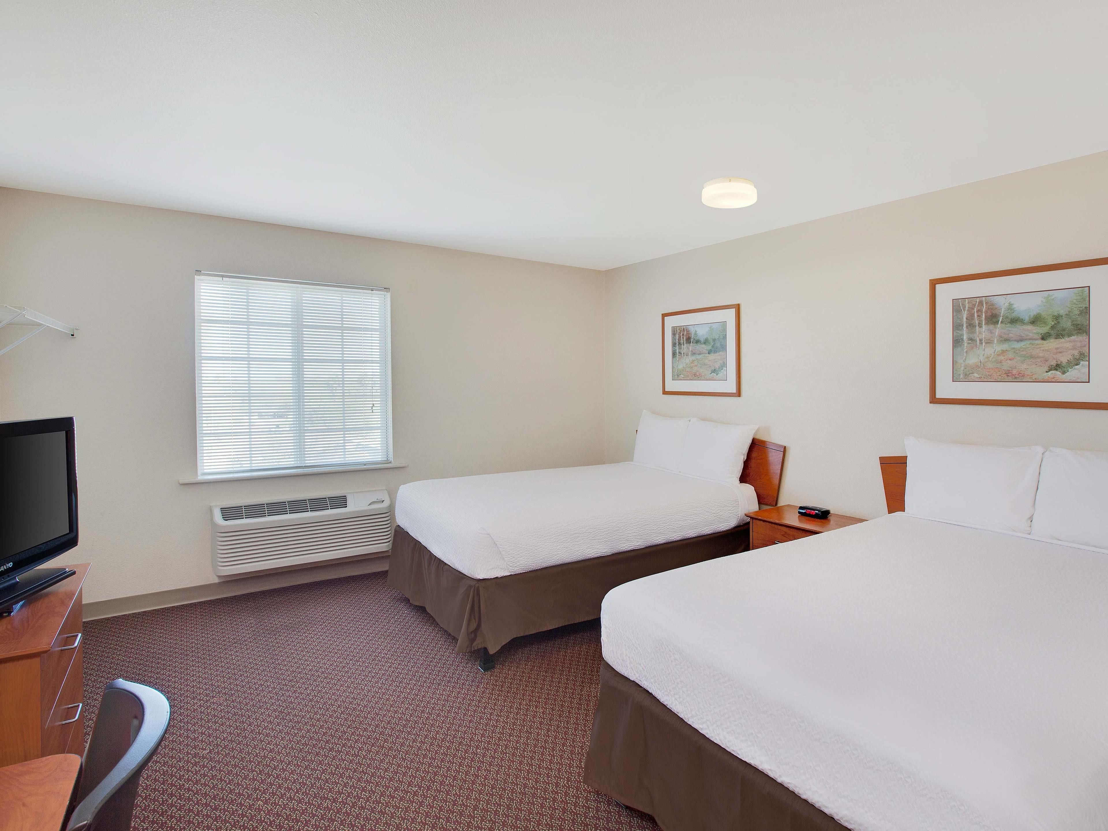 A hotel room with two beds, a TV, a heater, and a window with blinds.