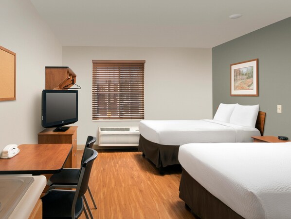 A hotel room with two beds, a desk, a chair, a television, and a window with blinds. - WoodSpring Suites Harlingen (Harlingen)