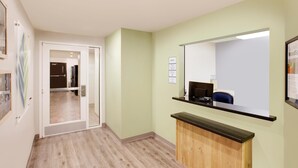 A hallway with a reception desk, a mirror, and a door leading to another room.