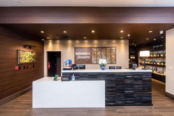 A hotel reception area with a modern design, featuring a reception desk, a welcome sign, and a bar area with shelves of bottles.