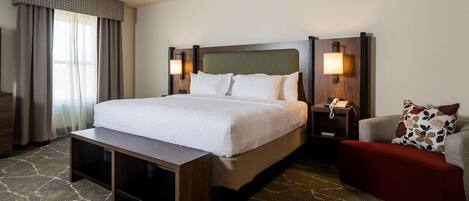 A hotel room with a large bed, bedside tables with lamps, a small sofa, and a bench.