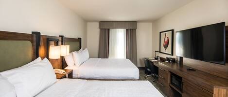 A hotel room with two beds, a TV, a desk, and a window with curtains.