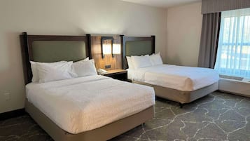 Een hotelkamer met twee bedden, een nachtkastje, een lamp en een raam met gordijnen.