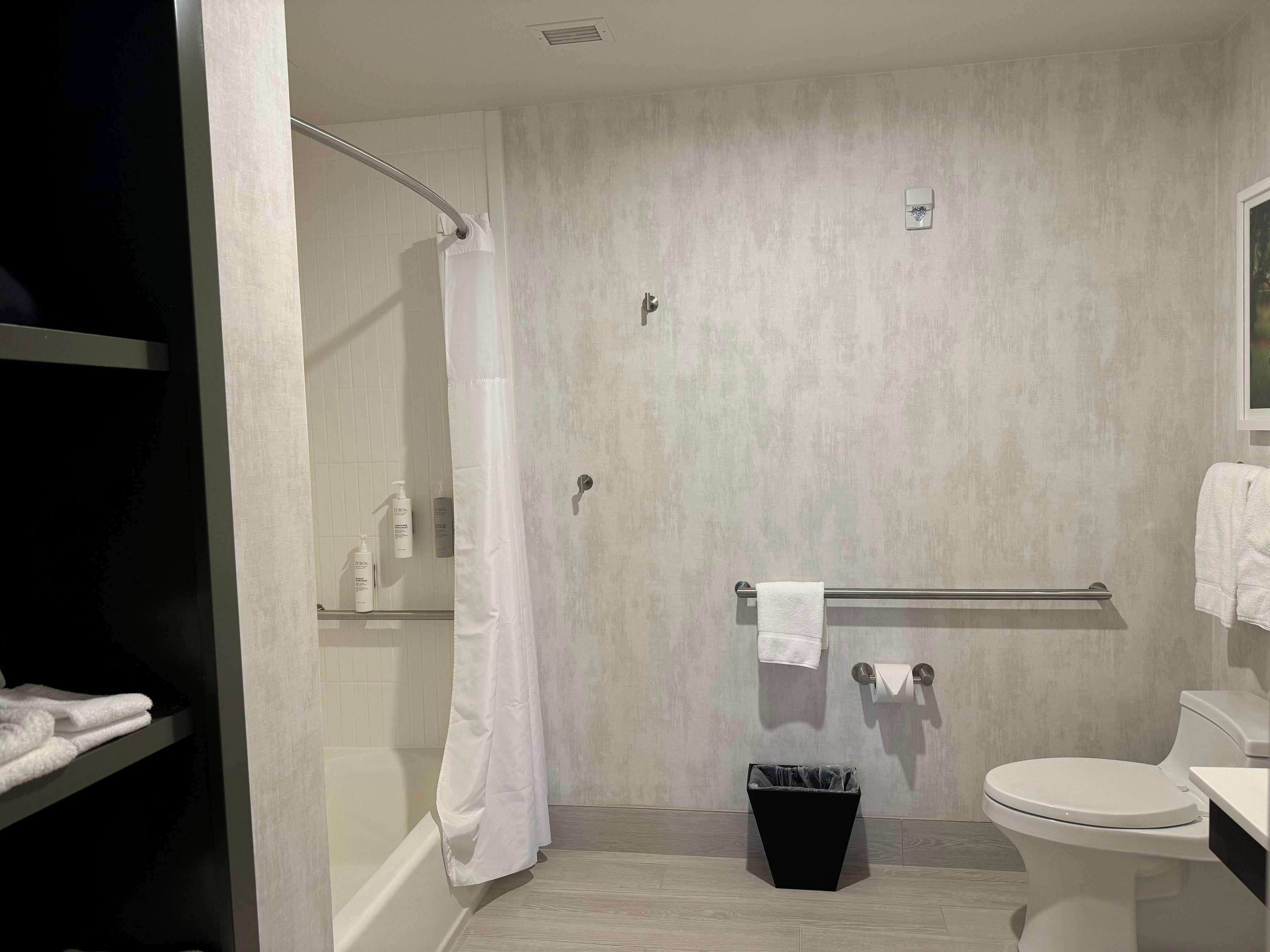 A modern bathroom with a glass shower enclosure, a toilet, a sink, and a trash bin.