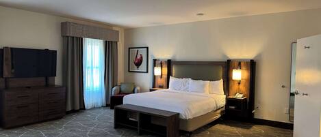 A hotel room with a large bed, a TV on a dresser, a desk, a chair, and a door.