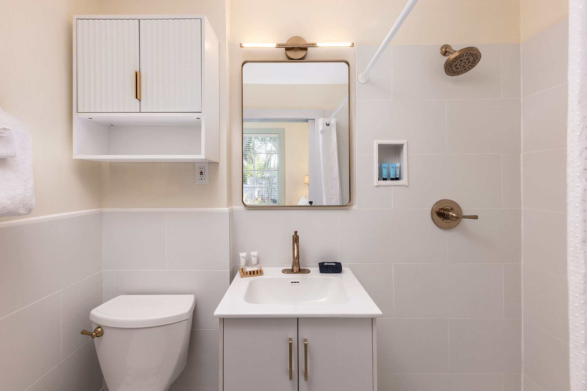 A bathroom with a toilet, sink, mirror, shower, and a cabinet with toiletries.