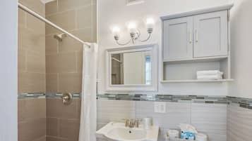 A bathroom with a shower, a sink, a mirror, and a cabinet.