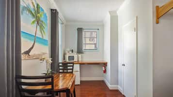 A compact room with a wooden dining table, chairs, a small kitchenette, a window with blinds, and a door.