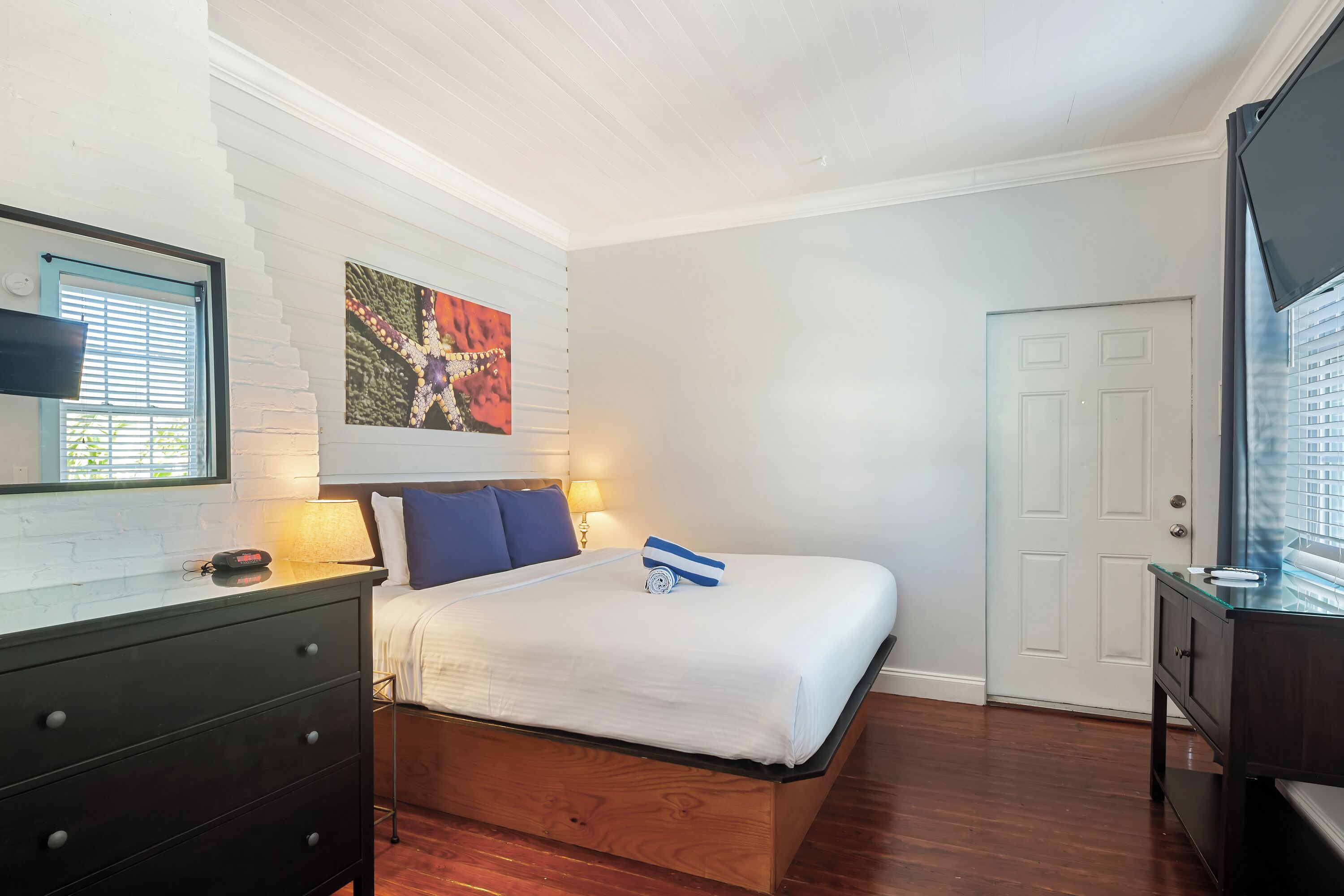 Quarto com cama de madeira, penteadeira, quadro na parede e porta.
