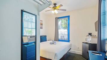 A hotel room with a bed, a desk, a ceiling fan, a microwave, and a refrigerator.