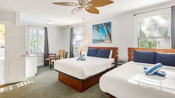 A hotel room with two beds, a ceiling fan, a beach-themed painting, and a view of the outdoors through the windows.