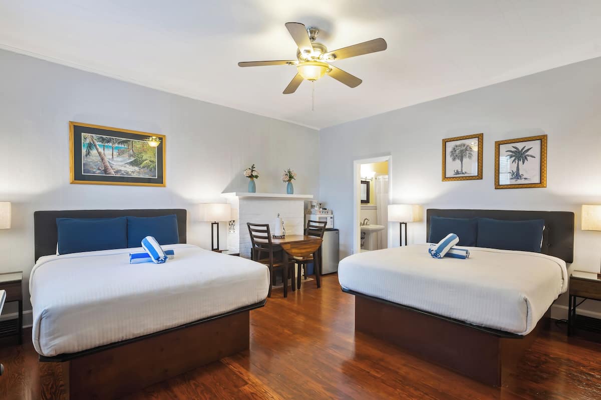 Une chambre d’hôtel avec deux lits, un ventilateur de plafond, un coin repas et des œuvres d’art accrochées aux murs.
