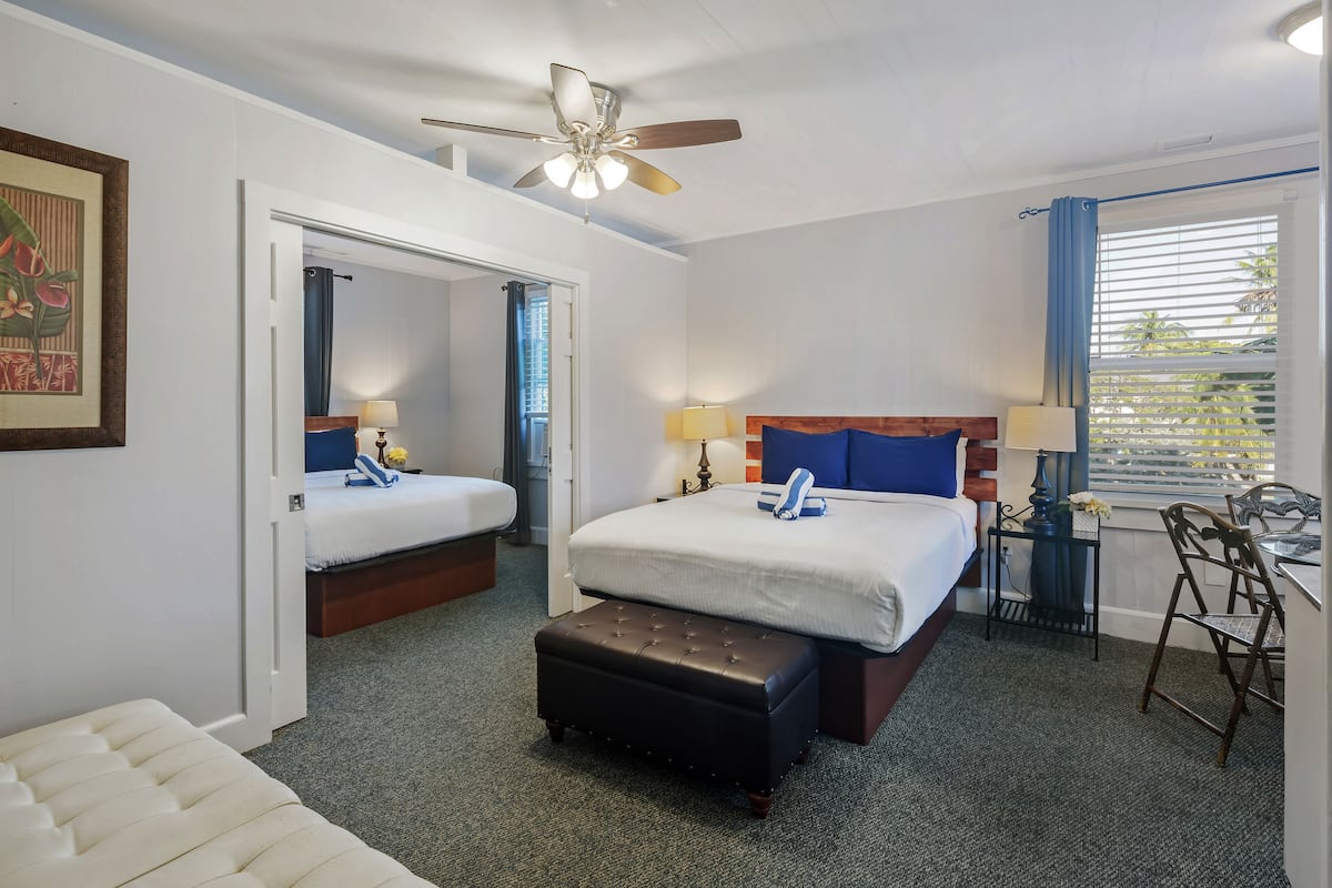 Une chambre d’hôtel avec deux lits, un ventilateur de plafond, un bureau avec une chaise et une fenêtre avec des stores.