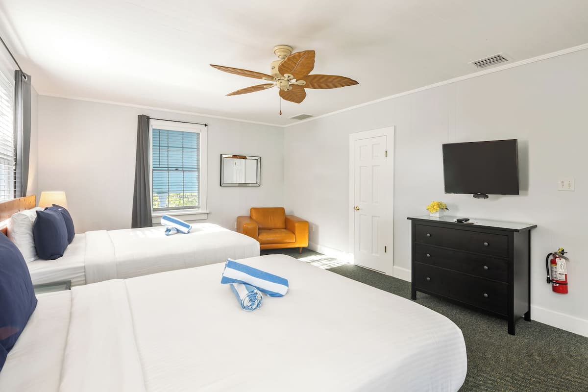 Une chambre d’hôtel avec deux lits, un ventilateur de plafond, une télévision, une commode et une chaise.