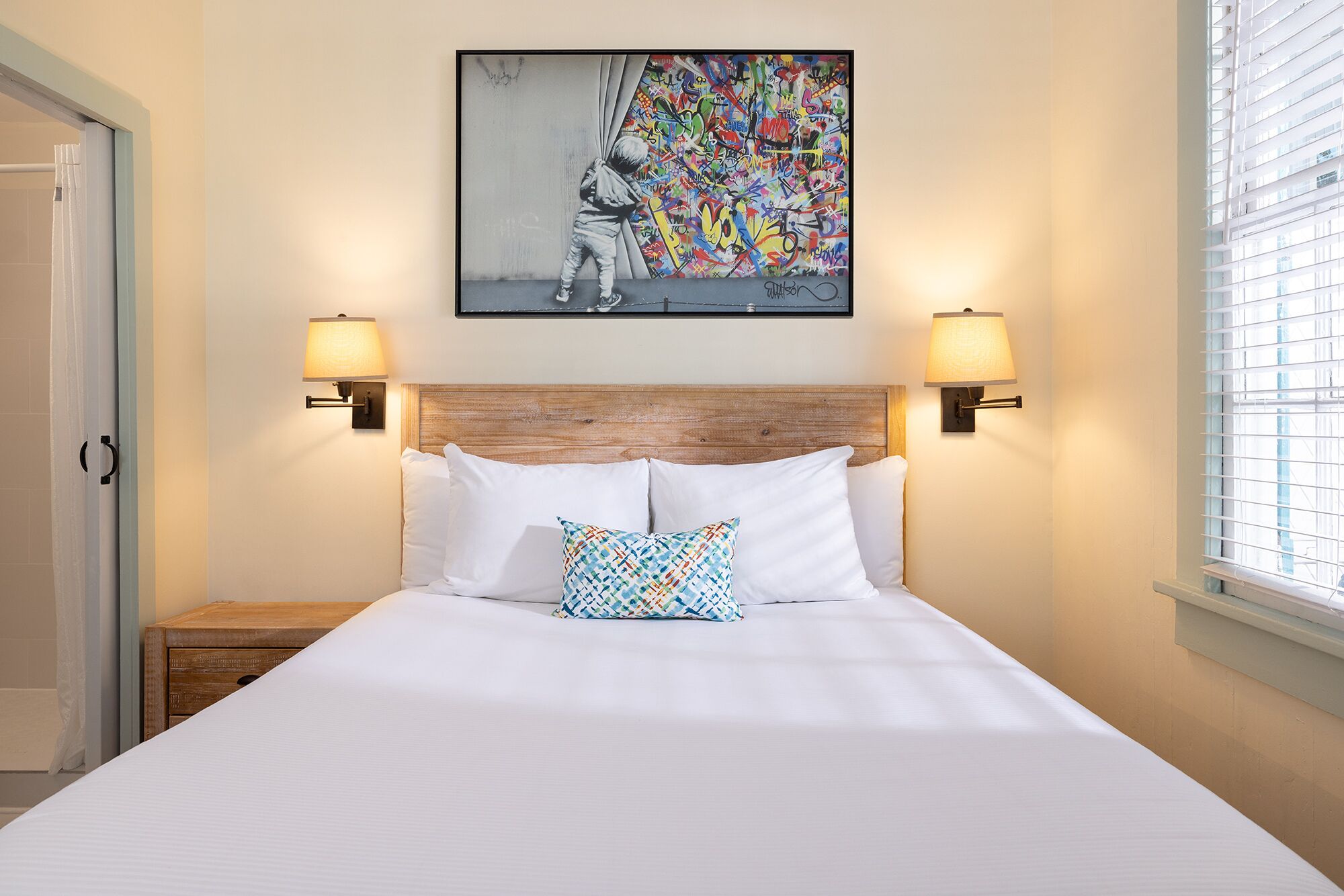 A hotel room with a bed, two bedside lamps, a headboard, and a large abstract painting on the wall.
