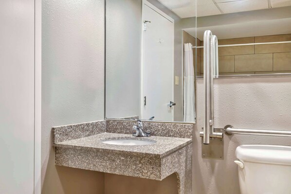 Un baño con lavamanos de granito, un espejo, inodoro y zona de ducha.