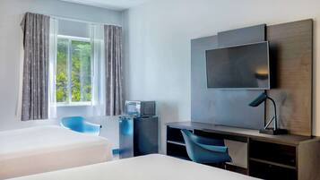 A modern hotel room with a bed, a desk with a computer, a TV, and a window with curtains.