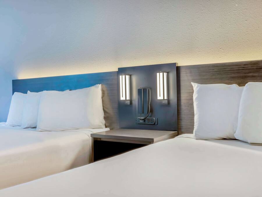 Quarto de hotel com duas camas, uma mesa de cabeceira e um telefone fixado na parede.
