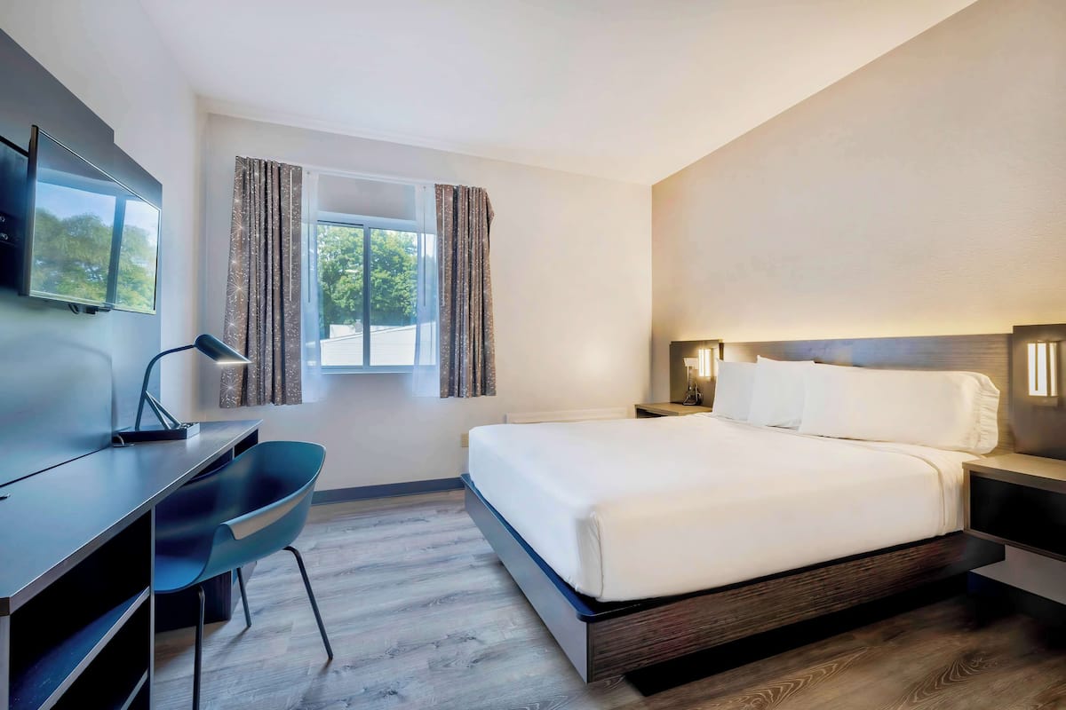 A modern hotel room with a bed, desk, chair, and a TV.