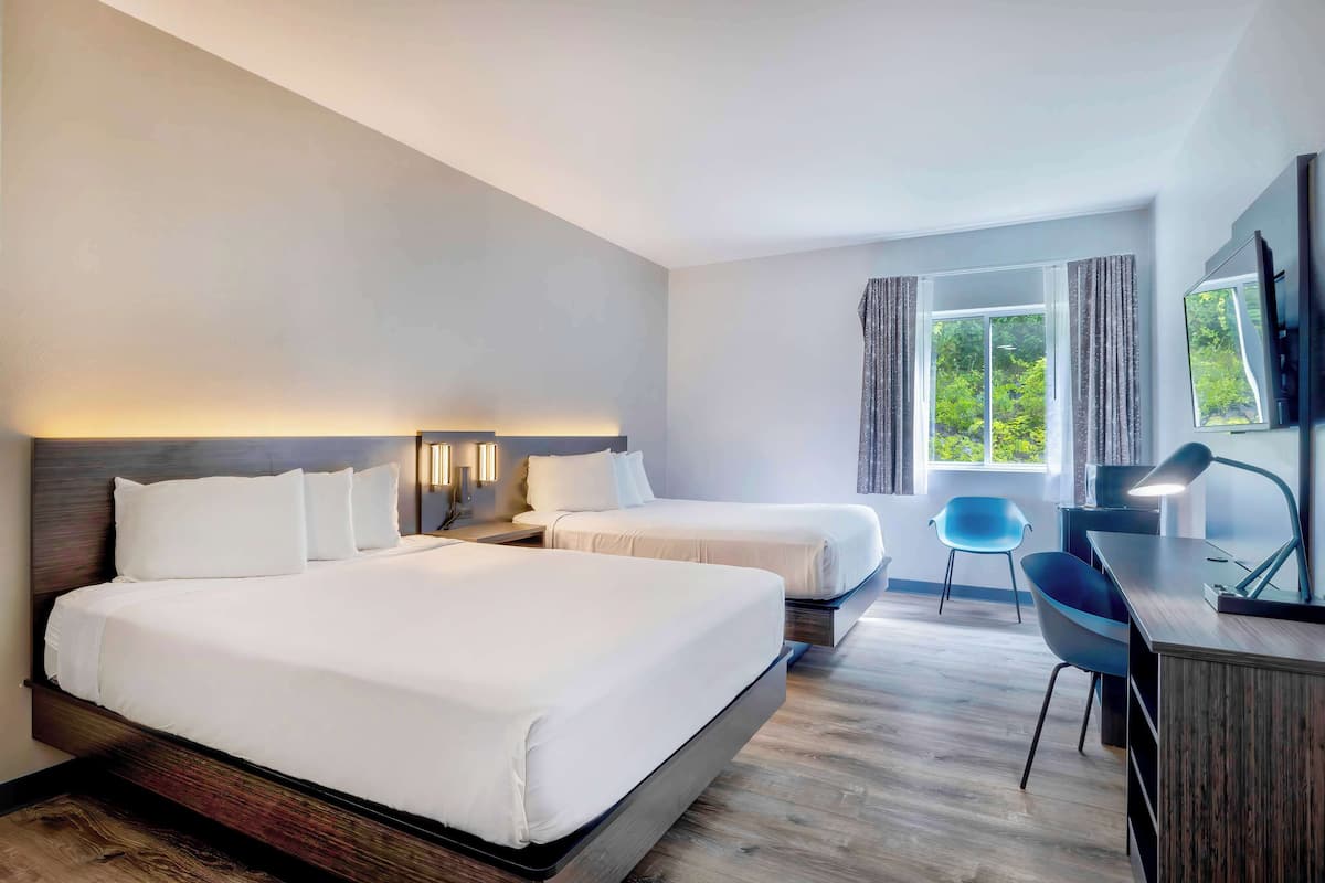 A hotel room with two beds, a desk, a chair, and a large window with curtains.