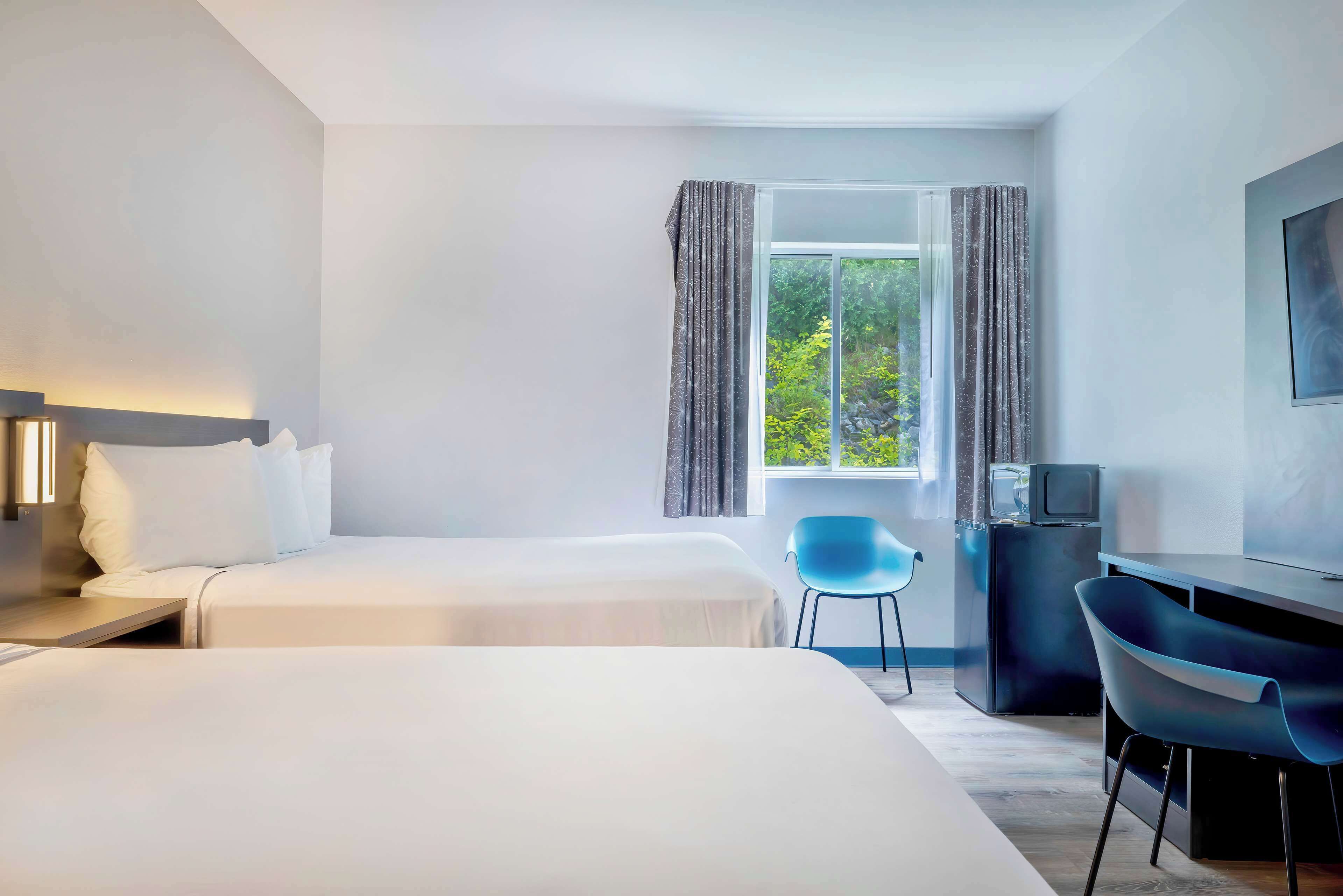 A hotel room with two beds, a desk with a chair, a television, and a window with curtains.