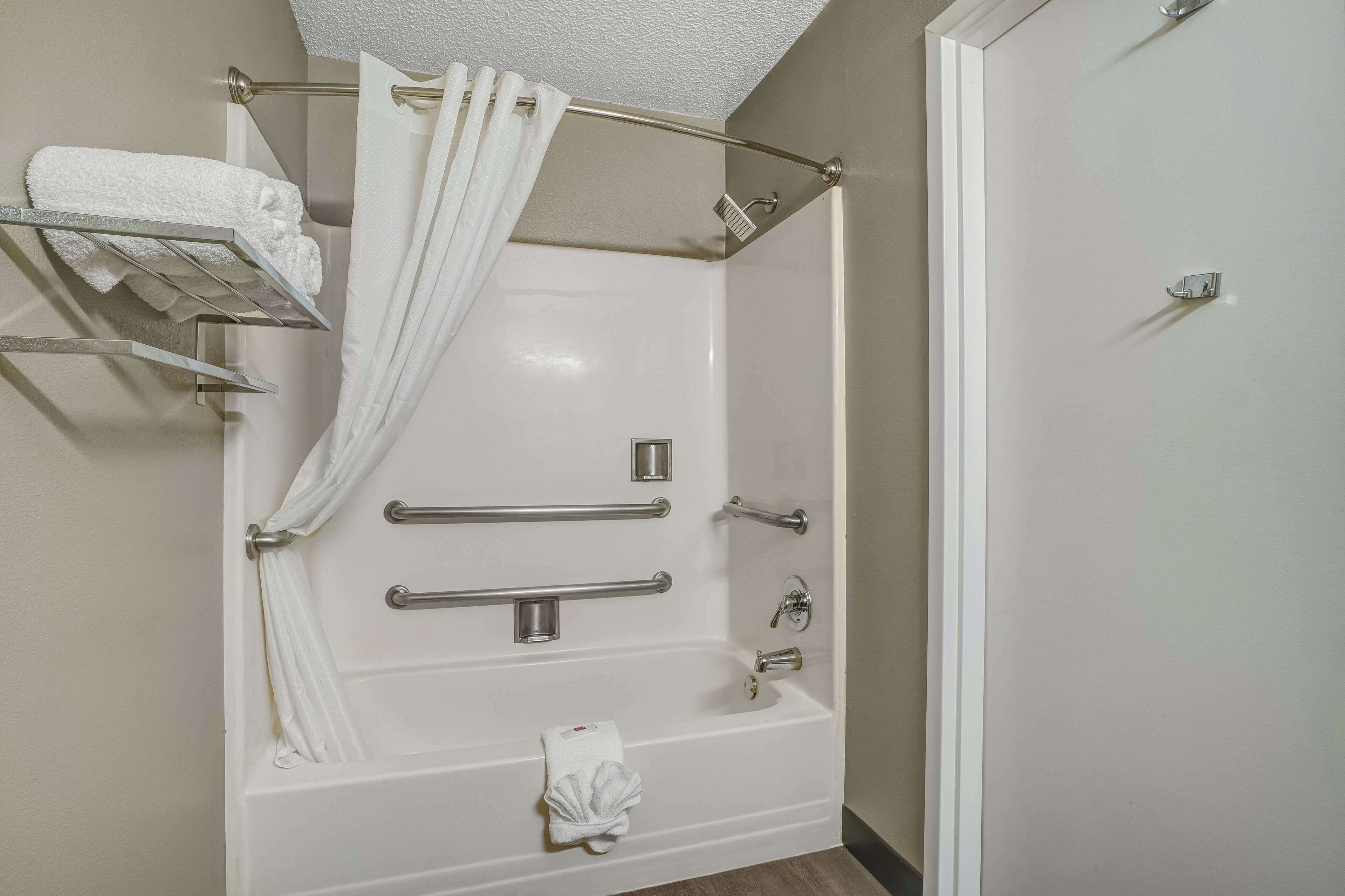 Un baño moderno con ducha a nivel, barras de apoyo, toallero y soporte para papel higiénico.