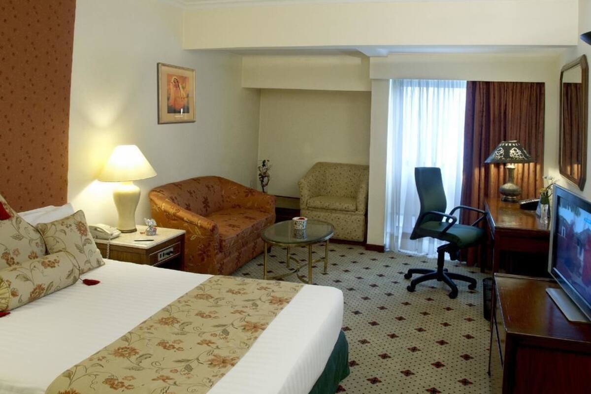 Habitación de hotel con una cama grande, un escritorio con televisor, una silla, una mesita y una lámpara.