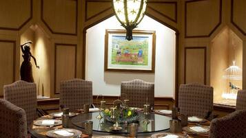 A conference room with a round table, patterned chairs, a chandelier, and a framed painting on the wall.