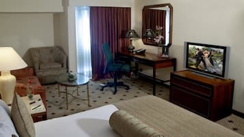 Een hotelkamer met een bed, een bureau, een stoel, een televisie en een klein tafeltje met een lamp.