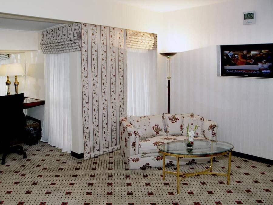 A living room with a sofa, a glass coffee table, a lamp, and a television on the wall.
