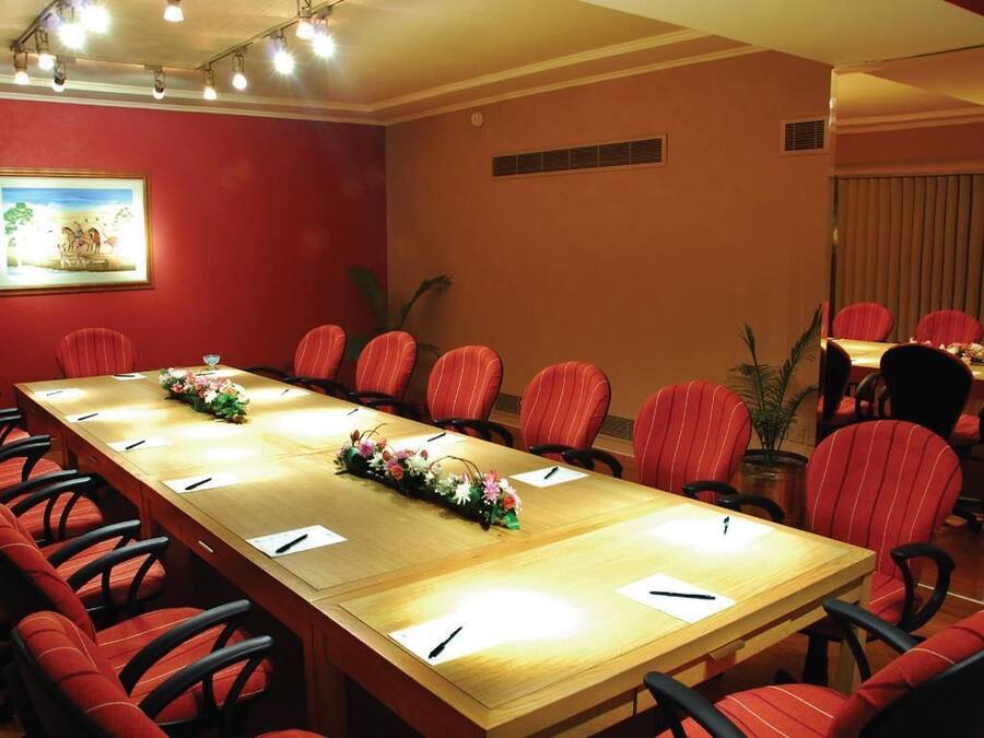 Una sala de conferencias con una larga mesa, sillas rojas y una decoración floral.