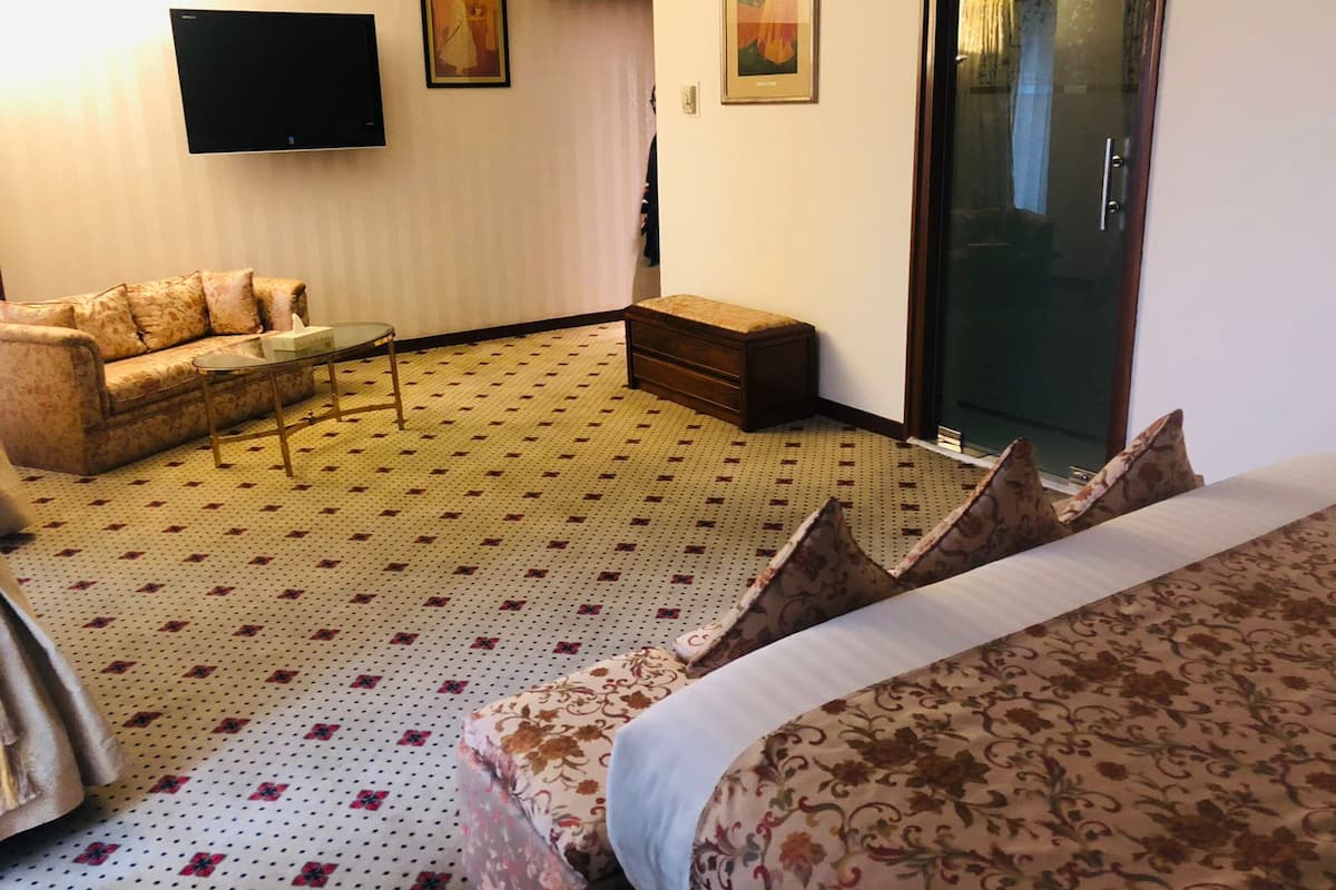 Habitación de hotel con sofá, una mesita, un banco, televisor y puerta corrediza.