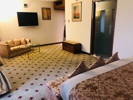 Habitación de hotel con sofá, una mesita, un banco, televisor y puerta corrediza.